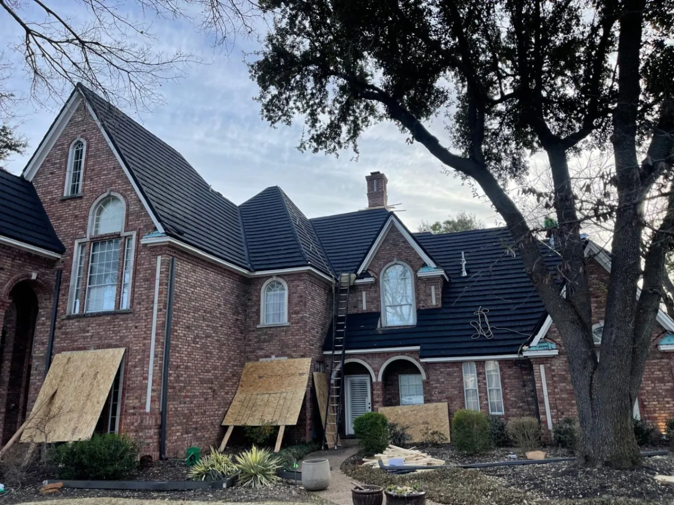 Brick Tudor-style home with black tile roof mid-installation